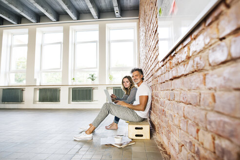 Geschäftsmann und Frau sitzen in einem Loft, benutzen einen Laptop und gründen ein Start-up-Unternehmen - HAPF02482