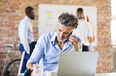 Businessman working in office talking on the phone, taking notes - HAPF02498