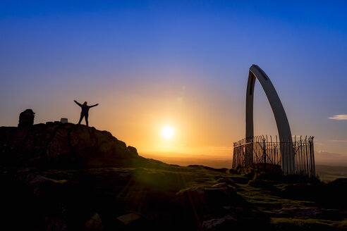 Großbritannien, Schottland, East Lothian, North Berwick, North Berwick Law, Walfischkieferknochenbogen, Sonnenuntergang, Touristin mit erhobenen Armen - SMAF00901