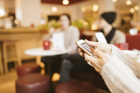 junge Frau tippt auf dem Display eines Smartphones in einem Café, lizenzfreies Stockfoto