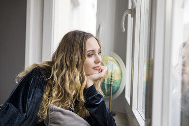 Portrait of daydreaming young woman looking through window - FMKF04646