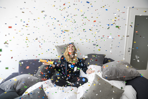 Laughing young woman having fun with flying confetti at home stock photo