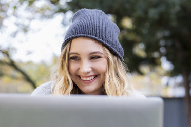 Porträt einer glücklichen jungen Frau, die einen Laptop im Freien benutzt - FMKF04655