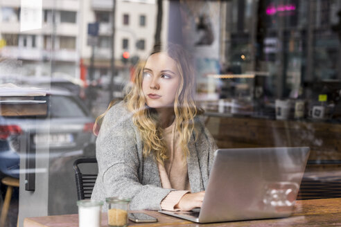 Porträt einer jungen Frau, die in einem Café an einem Laptop arbeitet - FMKF04656