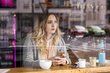 Porträt einer nachdenklichen jungen Frau in einem Café, die durch ein Fenster schaut - FMKF04657