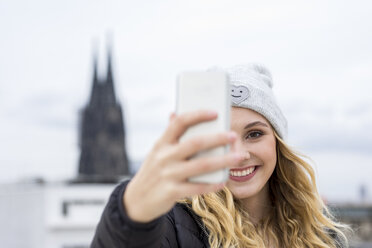 Deutschland, Köln, Porträt einer lachenden jungen Frau, die ein Selfie mit ihrem Smartphone macht - FMKF04661