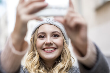 Porträt einer lachenden jungen Frau, die ein Selfie mit ihrem Smartphone macht - FMKF04662
