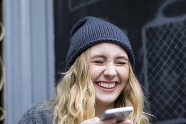 Porträt einer lachenden jungen Frau mit Smartphone - FMKF04664