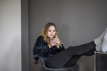 Portrait of young woman with hot beverage at home - FMKF04671