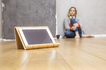 Tablet auf Tablet-Ständer auf dem Boden mit junger Frau im Hintergrund sitzend - FMKF04678