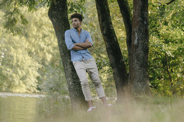 Young man in park leaning against a tree at the water - KNSF03170