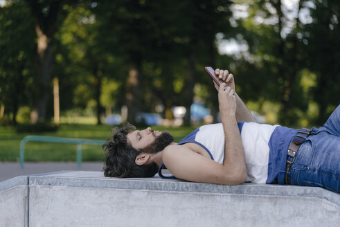Mann mit Mobiltelefon im Skatepark liegend - KNSF03175