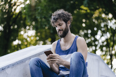 Mann mit Mobiltelefon im Skatepark sitzend - KNSF03179