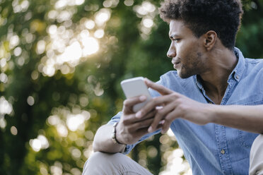 Young man with cell phone in park looking around - KNSF03183