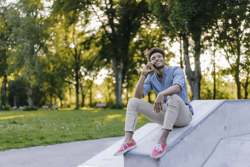 Lächelnder junger Mann mit Handy im Skatepark sitzend - KNSF03185