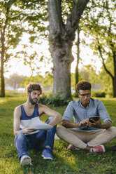 Zwei Freunde sitzen mit Handy und Papieren in einem Park - KNSF03196