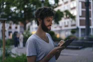 Mann schaut in der Abenddämmerung in der Stadt auf sein Phablet - KNSF03205