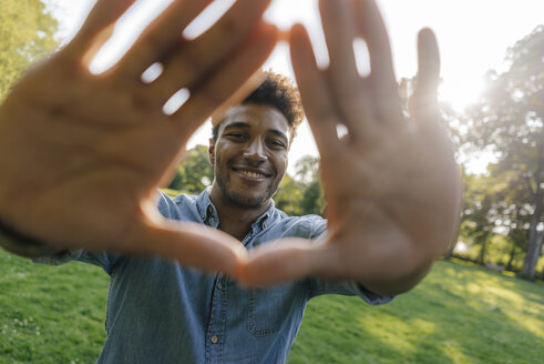 Porträt eines lächelnden jungen Mannes, der im Park einen Fingerrahmen macht - KNSF03218