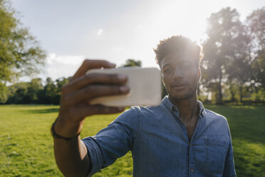 Young man holding cell phone in park at sunset - KNSF03219