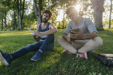 Zwei Freunde sitzen mit Handy und Papieren in einem Park - KNSF03222