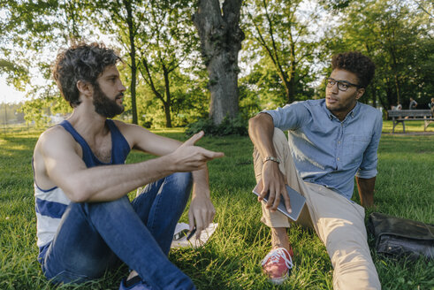 Zwei Freunde sitzen mit Handy und Papieren in einem Park und diskutieren - KNSF03224