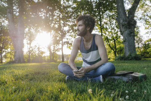 Mann sitzt mit Handy im Park und schaut sich um - KNSF03229