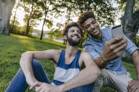 Zwei glückliche Freunde teilen sich ein Mobiltelefon in einem Park, lizenzfreies Stockfoto