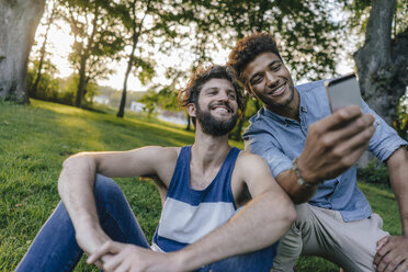 Zwei glückliche Freunde teilen sich ein Mobiltelefon in einem Park - KNSF03235