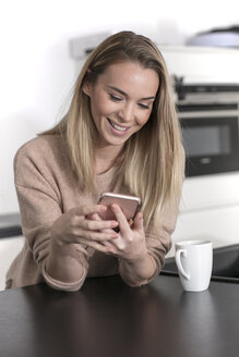 Porträt einer lächelnden blonden Frau, die zu Hause ein Mobiltelefon benutzt - GDF01174