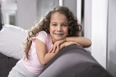 Porträt eines lächelnden kleinen Mädchens mit Zahnlücke auf der Couch - GDF01181