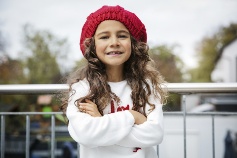 Porträt eines lächelnden kleinen Mädchens mit Zahnlücke und roter Wollmütze, lizenzfreies Stockfoto