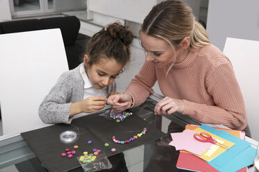 Mother and little daughter stringing beads for creating a necklace - GDF01190