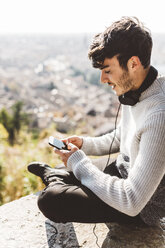 Italy, Verona, tourist using smartphone, headphones - GIOF03584