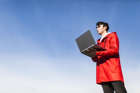 Blauer Himmel, junger Mann mit Laptop - GIOF03587