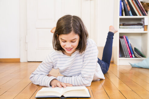 Smiling girl lying on the floor reading book - LVF06497