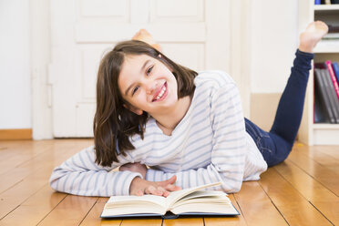 Portrait of happy girl lying on the floor with book - LVF06498