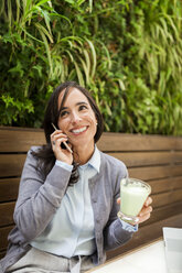 Lächelnde Frau am Handy im Gartencafé - VABF01391
