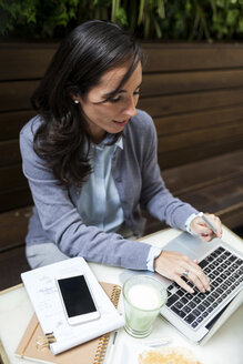 Beschäftigte Geschäftsfrau, die in einem Café im Freien am Laptop arbeitet - VABF01393