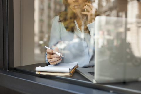 Beschäftigte Geschäftsfrau bei der Arbeit hinter einer Fensterscheibe, lizenzfreies Stockfoto