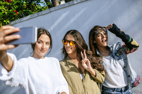 Drei lächelnde junge Frauen machen ein Selfie mit Smartphone, lizenzfreies Stockfoto