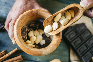 Man's hands pouring almonds in a wooden bowl with chocolate - KIJF01777