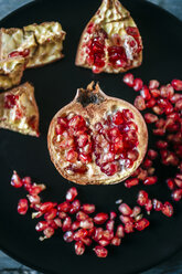 Half of pomegranate and pomegranate seed on black plate, close-up - KIJF01784