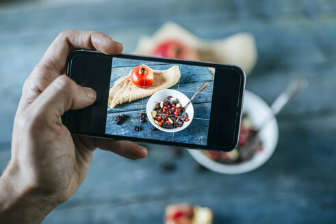 Man's hand taking a picture with smartphone of bowl with dessert of almonds, pomegranate and chocolate - KIJF01795