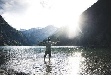 Austria, Tyrol, hiker standing with outstretched arms in mountain lake - UUF12481