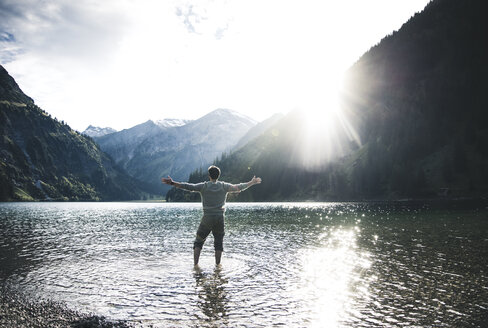 Österreich, Tirol, Wanderer steht mit ausgestreckten Armen im Bergsee - UUF12481