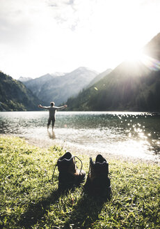 Österreich, Tirol, Wanderschuhe und Mann mit ausgestreckten Armen im Bergsee stehend - UUF12483