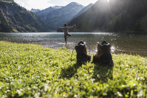 Österreich, Tirol, Wanderschuhe und Mann in Yogastellung im Bergsee - UUF12485