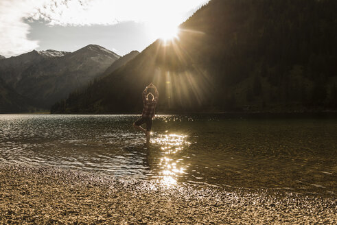 Österreich, Tirol, Wanderer in Yogapose beim Erfrischen im Bergsee - UUF12487