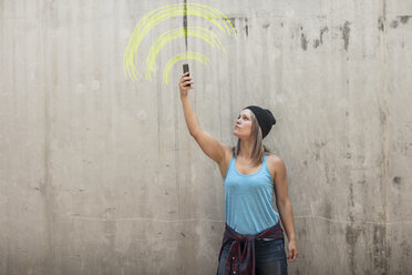 Frau hält Telefon auf der Suche nach Signal mit wifi Zeichen in gelber Kreide auf Betonwand gezeichnet - ZEF14874
