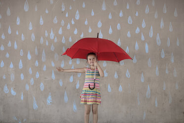 Mädchen, das einen roten Regenschirm hält, steht neben einer Betonwand mit Kreidezeichnungen von Regentropfen - ZEF14893